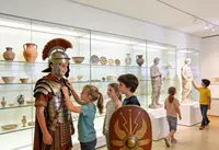 Kinder probieren römische Rüstung in einer Museumsausstellung aus und betrachten Ausstellungsstücke.