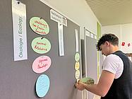 Ein Schüler befestigt beschriftete Karten zu ökologischen Themen an einer Pinnwand.