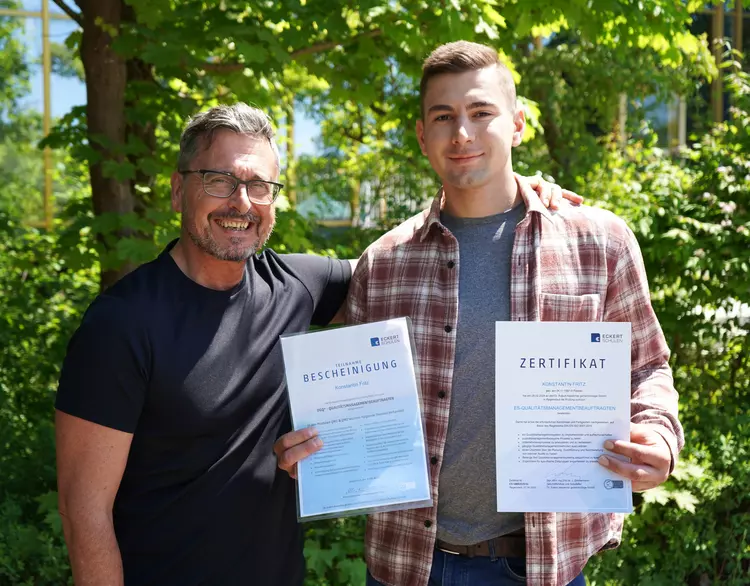 Foto von Coach und Teilnehmer. Teilnehmer hält seine Zertifikate in der Hand.