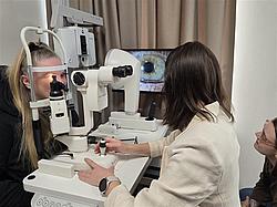 Anwendung moderner Diagnosetechnik Eine Teilnehmerin sitzt am Untersuchungsgerät, während eine Dozentin Einstellungen vornimmt und eine weitere Person zuschaut.