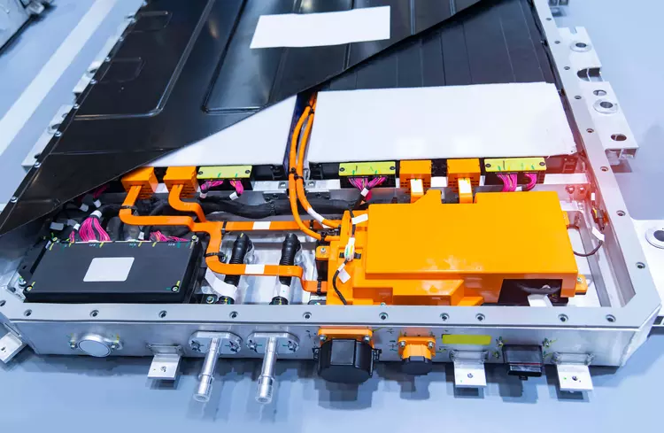 Geöffnete Hochvoltbatterie eines Elektrofahrzeugs mit sichtbaren Batteriemodulen, orangefarbenen Hochvoltleitungen, Steckverbindungen und Steuerungskomponenten.