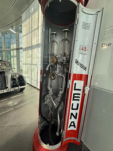 Historische rote LEUNA-Zapfsäule mit freigelegter Technik im Audi Museum Ingolstadt, im Hintergrund ein Oldtimer.