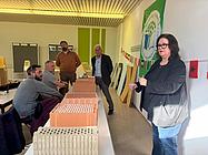 Eine Dozentin erklärt verschiedene Baustoffe anhand von Modellen, während Teilnehmende aufmerksam zuhören.