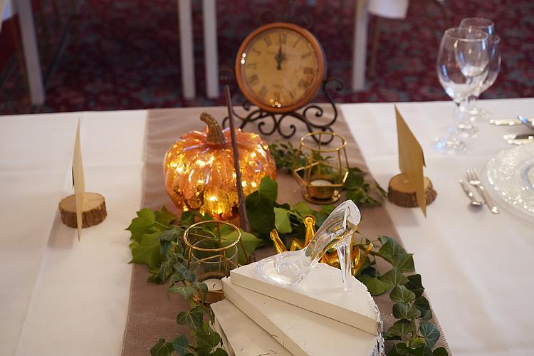 Ein Abend wie im Märchen Detail eines festlich dekorierten Tisches im Cinderella-Motto mit gläsernem Schuh, Kürbislampe, Uhr und goldener Krone.