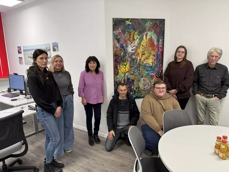 Teilnehmende des Kreativkurses und Dozent Heinrich Brunner stehen gemeinsam vor dem fertiggestellten, abstrakten Gemälde im Büro des BFW-Sekretariats.