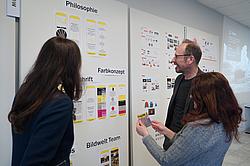 Dozent und Teilnehmerinnen betrachten Präsentationsboards mit Philosophie- und Farbkonzept im Mediengestalter-Projekt „Inge unterwegs“ an den Eckert Schulen.