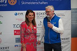 Ansprache Golsponsor: Andrea Radlbeck in Vertretung für das Berufsförderungswerk Eckert Ansprache Golsponsor: Andrea Radlbeck in Vertretung für das Berufsförderungswerk Eckert. Andrea Radlbeck steht in einem roten Kleid vor der Sponsorentafel und wird von einem Vertreter des Rotary Clubs interviewt.