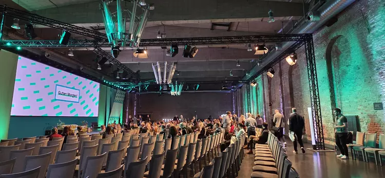 Blick in einen großen Veranstaltungssaal mit Bühne, Leinwand und Publikum bei der Work Awesome 2025.