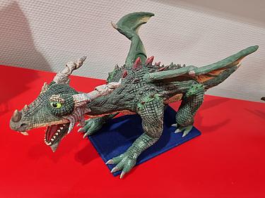 Detailreiche, grüne Drachenfigur mit Flügeln und geöffnetem Maul auf blauem Sockel.