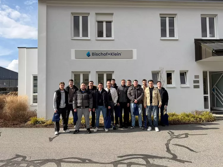 Teilnehmer des Lehrgangs stehen vor dem Firmengebäude von Bischof + Klein und posieren für ein Gruppenfoto.
