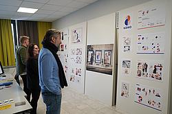 Teilnehmer und Dozenten analysieren gemeinsam die ausgearbeiteten Corporate-Design-Elemente an der Präsentationswand.