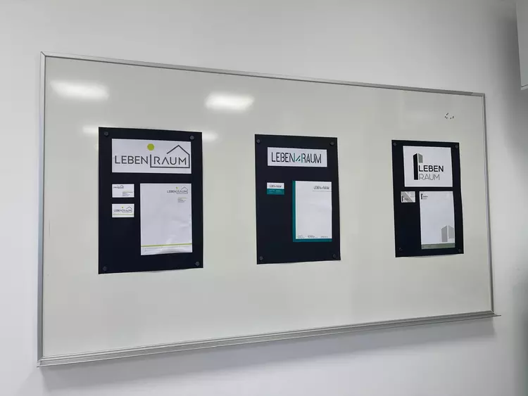Mehrere Designentwürfe für ein Logo und Geschäftsausstattung hängen an einer Präsentationswand.
