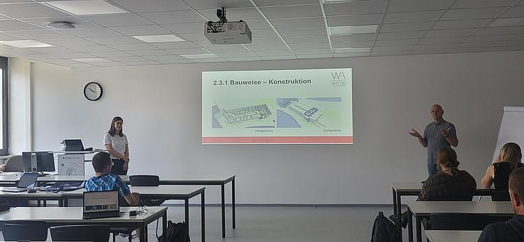 Architekt und Kollegin präsentieren Baupläne vor Studierenden im Klassenzimmer der Eckert Schulen
