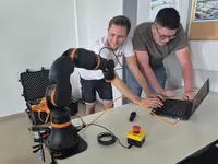 IGUS 1 Zwei Schüler arbeiten gemeinsam mit einem schwarzen Roboterarm und einem Laptop an einem Tisch.