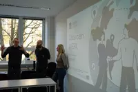 ChancenWerk: Zusammenarbeit, die wirkt Drei Beteiligte stehen vor einer projizierten Präsentation des Projekts ChancenWerk an den Eckert Schulen und tauschen sich aus.