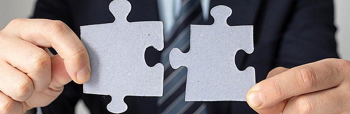 Person im Anzug hält zwei Puzzleteile, die aufeinanderpassen