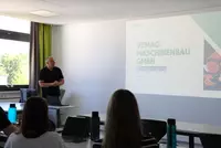 Thomas Dippel hält einen Vortrag vor angehenden Lebensmittelverarbeitungstechnikern. Auf der Präsentationsfolie ist die VEMAG Maschinenbau GmbH zu sehen.
