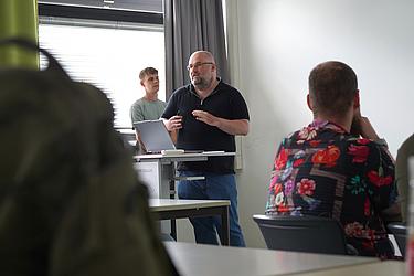 Zwei Teilnehmende stehen während einer Präsentation vor der Gruppe im Seminarraum.