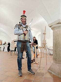 Mann in römischer Rüstung mit Helm und Schwert steht in einem Ausstellungsraum des Burgmuseums Parsberg.