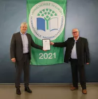 Markus Johannes Zimmermann (Geschäftsführer und Schulleiter der Dr. Eckert Akademie, links) und Gerald Saule (Head of Vocational Training International und Umweltbeauftragter, rechts) mit der Flagge und Auszeichnung zur Umweltschule. Foto: Eckert Schulen 