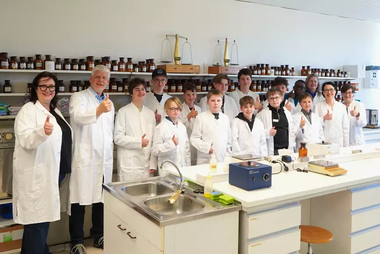 Gruppe von Schülern und Lehrkräften im Labor zeigt Daumen hoch.