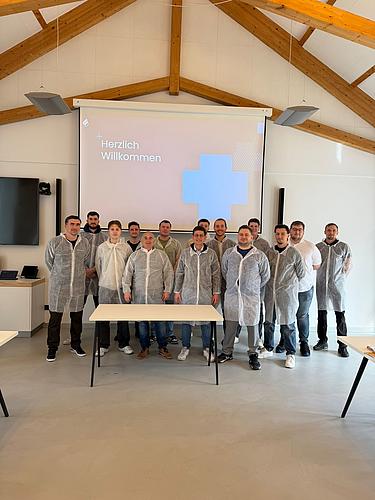 Gruppenfoto von Teilnehmern in Schutzkleidung vor einer Präsentationsfläche mit Begrüßungsfolie während der Betriebsbesichtigung.