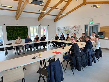 Gruppe angehender Industriemeister sitzt in U-Form an Tischen und hört aufmerksam zu, während eine Schulung in einem hellen Raum stattfindet.