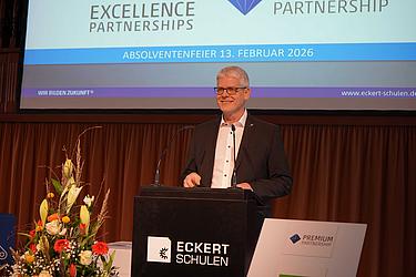 Herr Zimmermann bei seiner Rede zur Absolventenfeier 2026 Ein Mann mit Brille steht am Rednerpult der Eckert Schulen und spricht bei einer Absolventenfeier.