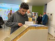 Ein Schüler untersucht ein Baumodell mit verschiedenen Schichten und Materialien aus nächster Nähe.