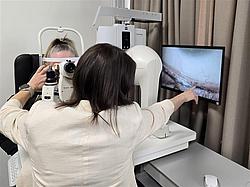 Praxis am Spaltlampenmikroskop Eine Teilnehmerin wird am Spaltlampenmikroskop untersucht, während eine Dozentin die Aufnahme auf einem Monitor erklärt.