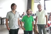 Lehnhardt Vortrag Drei Männer stehen nebeneinander im Vordergrund eines Klassenzimmers, während im Hintergrund Teilnehmer an Tischen sitzen und dem Geschehen aufmerksam folgen.
