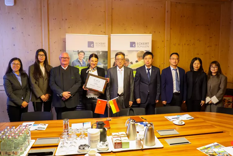 Gruppenfoto der chinesischen Delegation und ihrer Gastgeber bei den Eckert Schulen in Regenstauf. In der Mitte hält Andrea Radlbeck die gerahmte Tafel „Sino-German Qinling Workshop“.