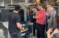 Gruppe beobachtet Demonstration einer Offsetdruckmaschine durch einen Mitarbeiter in einer Druckerei.
