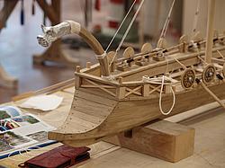 Detail eines hölzernen Modells eines römischen Schiffes mit Rudern und Verzierungen.