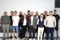 Gruppenfoto bei der Projektbesprechung Gruppenfoto von sechs Personen in unterschiedlicher Business-Kleidung vor einer weiß gestrichenen Wand mit dekorativen Farbstreifen. Alle stehen nebeneinander und lächeln in die Kamera.