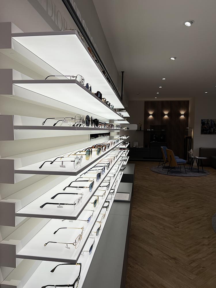 Brillenpräsentation auf hell beleuchteten Regalböden in einem modernen Optikgeschäft.