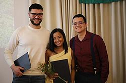 Drei Personen stehen nebeneinander, halten ihre Mappen und Blumen und lächeln nach der Zertifikatsvergabe.