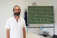 Teilnehmer eines Deutschkurses an den Eckert Schulen steht lächelnd im Unterrichtsraum vor einer Tafel mit deutschem Text.