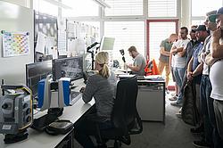 Teilnehmende eines Besuchs blicken in ein Planungsbüro mit mehreren Bildschirmen und modernen Vermessungsgeräten.