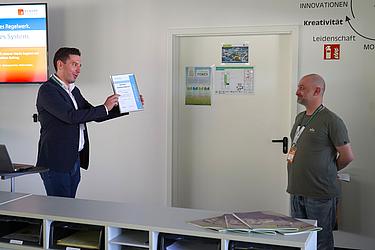 Übergabe eines Zertifikats an einen Teilnehmer während einer Präsentation.