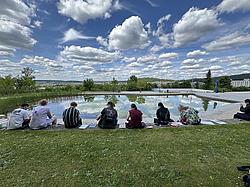 Studierende der Kreativ-Gruppe sitzen am Teich des Campus Regenstauf und arbeiten bei sonnigem Wetter an Zeichnungen und Projekten.