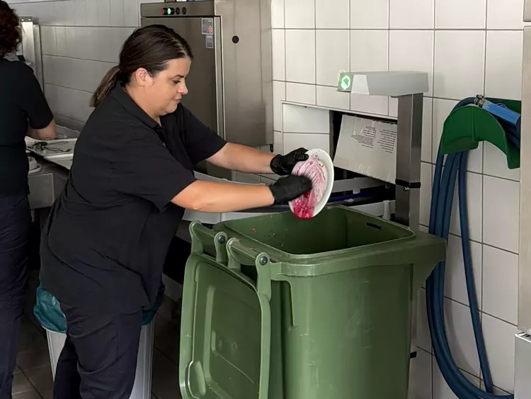 Eine Mitarbeiterin leert die Überreste des Mittagessens im Mülleimer aus.