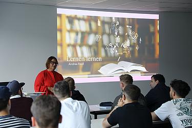 Andrea Riedl steht vor einer Projektionswand mit der Folie „Lernen lernen“ und erklärt den Teilnehmenden Strategien für erfolgreiches Lernen.