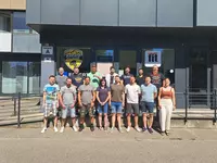 Abschluss mit Teamgeist – Gruppenfoto vor dem Trainingszentrum Eine Gruppe von 18 Personen – Männer und Frauen – steht in zwei Reihen für ein Gruppenfoto vor einem modernen Gebäude mit Glasfassade. Hinter ihnen sind die Logos „Karate Altinger“ und „Clever Fit“ sichtbar. Die Stimmung ist freundlich und sommerlich.