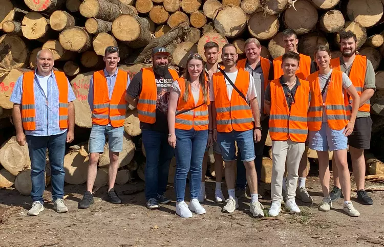 Binderholz Tirol Gruppe der Holztechnik-Studierenden mit Sicherheitswesten vor Holzstapeln bei der Firma Binderholz.