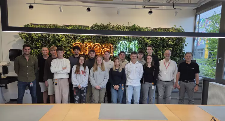 Gruppenfoto einer Ausbildungsgruppe von Aumovio mit Dozenten des Berufsförderungswerks Eckert in einem modernen Schulungsraum. Die Teilnehmenden stehen gemeinsam vor einer begrünten Wand mit leuchtendem Schriftzug „area01“ und blicken in die Kamera.
