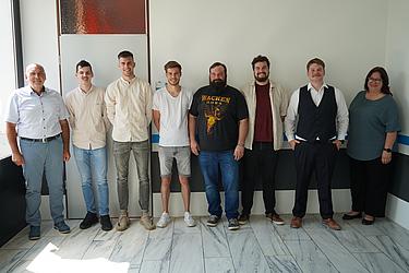 Ein Gruppenfoto von 8 Personen vor einer weißen Wand.
