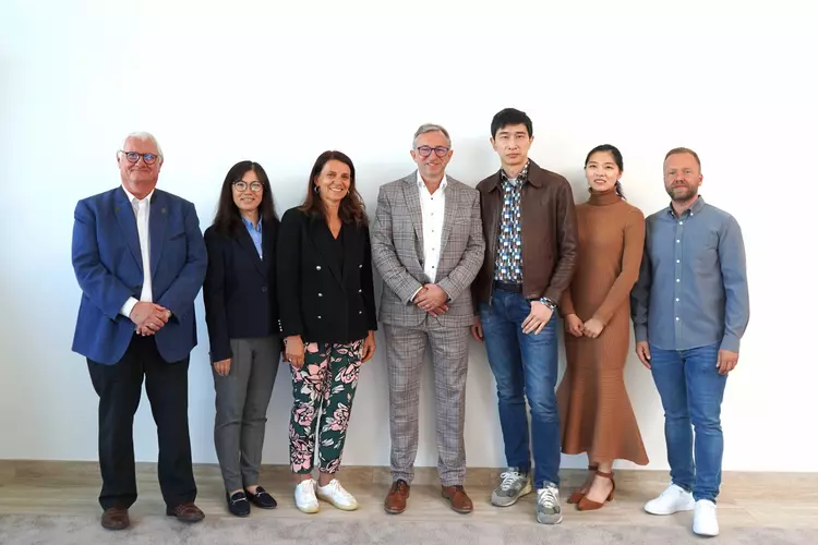 Sieben Personen stehen vor einer weißen Wand und schauen freundlich in die Kamera.