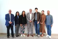 Sieben Personen stehen vor einer weißen Wand und schauen freundlich in die Kamera.