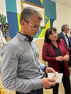Fairschenkladen Ein Mitarbeiter der Eckert Schulen steht im Fairschenkladen und schaut sich konzetriert die Postkarte mit dem System hinter dem Fairschenken an.